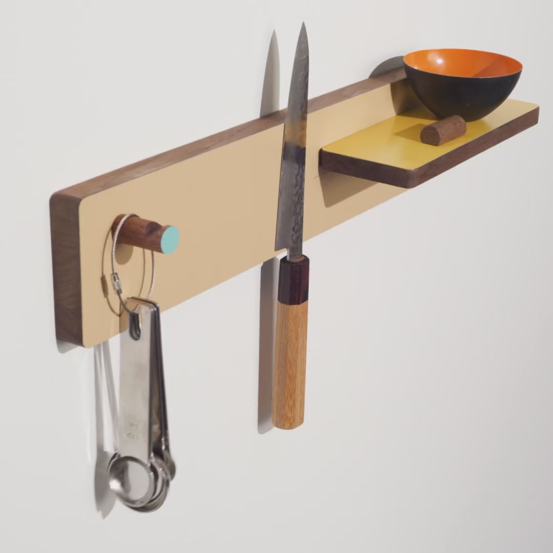 The Knife Rack is a wall mounted magnetic panel that holds knives(and&nbsp; protects their edge), a shelf for key seasoning and a hook for a potholder or favorite utensil. It's hard -working and easy on the eyes. In solid walnut with powder-coated magnetic components.